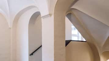 A corridor with white walls and arches, a staircase, and a view of the outside.