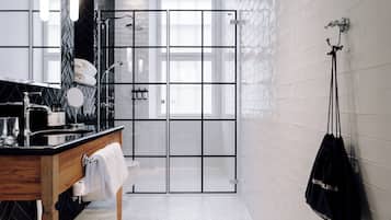 Un baño moderno con ducha de azulejos blancos y negros, tocador de madera y una bolsa colgada.