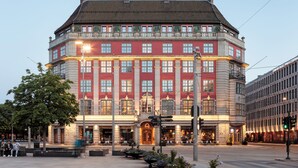 Et stort, flereetagers hotel med en markant indgang, udendørs siddeområde og en veloplyst facade.