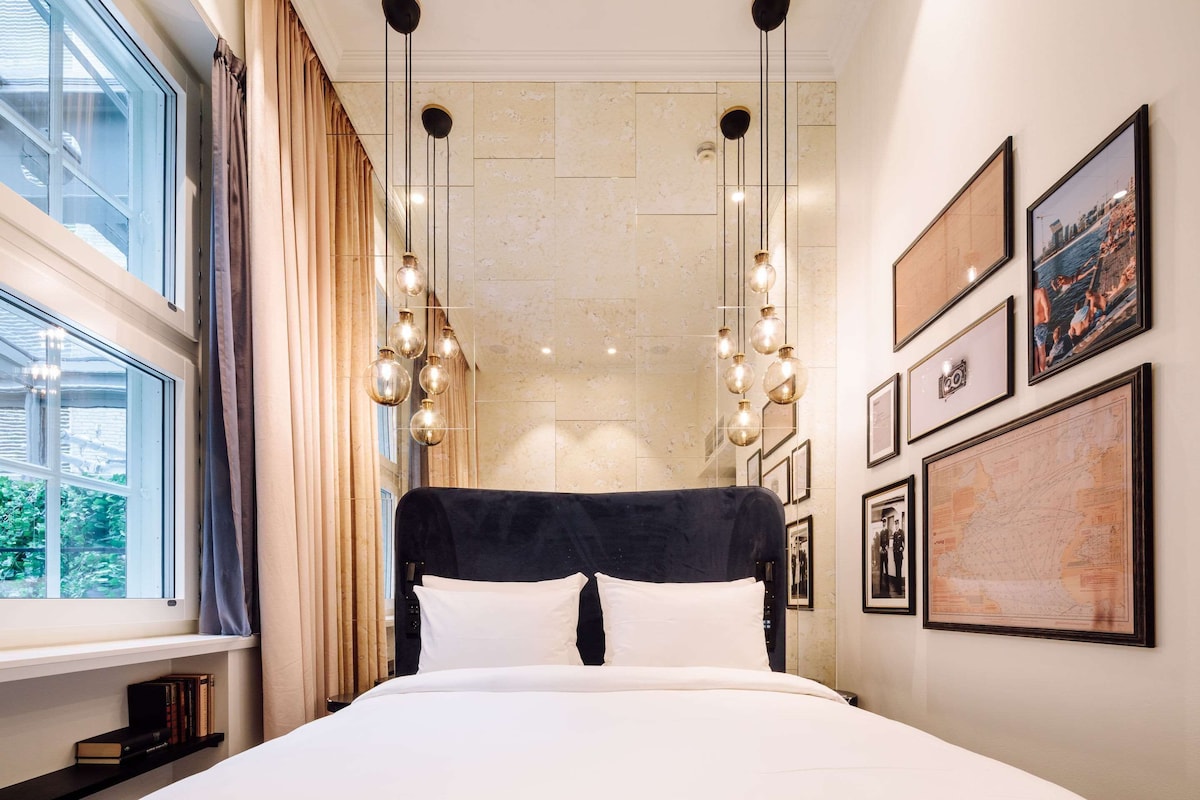 Un dormitorio con una cama grande, una ventana con cortinas e iluminación instalada en la pared.