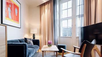 Un salon moderne avec un canapé bleu foncé, une petite table sur laquelle est posé un vase de fleurs, une chaise en bois et un téléviseur.