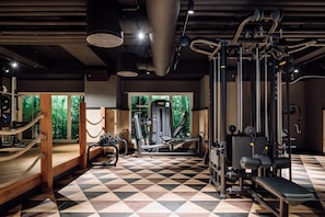 A gym with a checkered floor, various exercise machines, and a view of greenery through the windows.