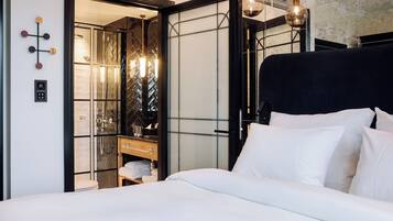 Una habitación de hotel moderna con una cama grande, un vestidor amplio y un baño con cabina de ducha de vidrio.