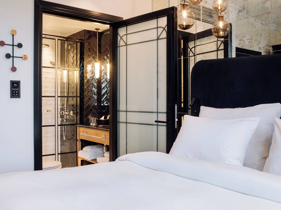 Una habitación de hotel moderna con una cama grande, un vestidor amplio y un baño con cabina de ducha de vidrio.