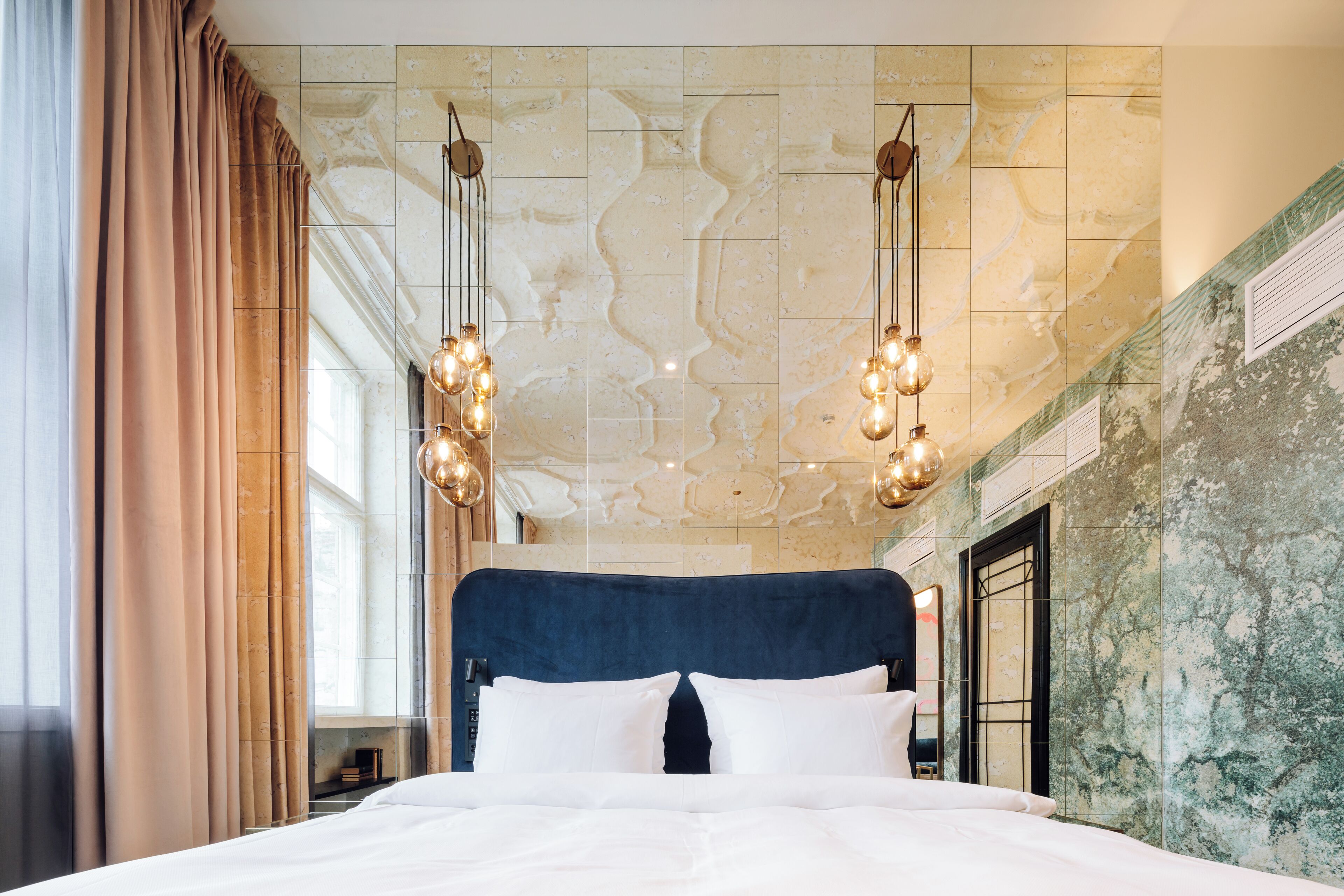 A large bed with a dark headboard, white bedding, and hanging light fixtures.