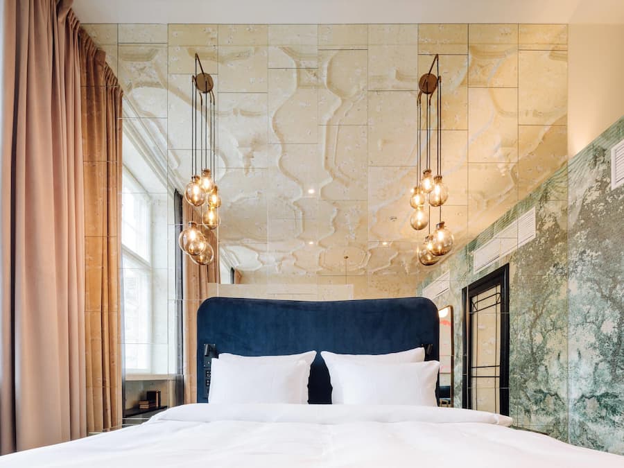 A large bed with a dark headboard, two hanging light fixtures, and a marble-patterned ceiling.