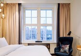 A hotel room with a large window, a bed, a chair, and a desk.