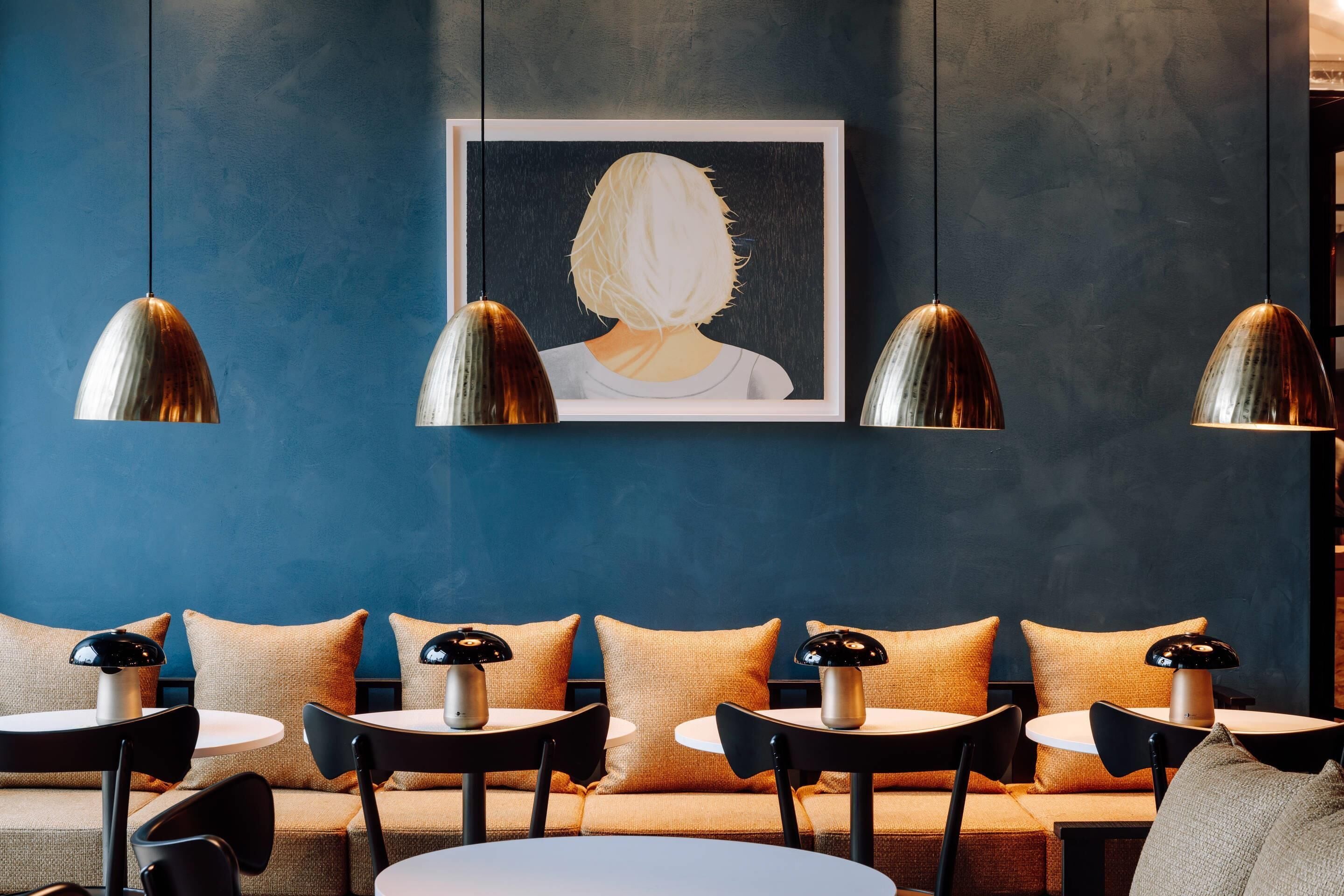 A modern interior with a blue wall, a framed artwork, and a seating area with tables and chairs.