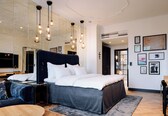 A modern hotel room with a large bed, bedside tables, a desk, and a seating area.