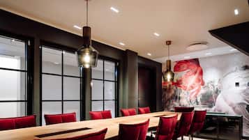 Une salle de conférence avec une longue table, des chaises rouges et des luminaires suspendus.