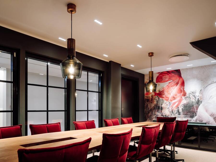 A conference room with a long table, red chairs, and pendant lighting.