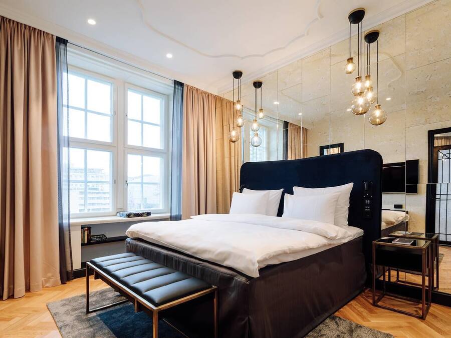 Une chambre d’hôtel moderne, dotée d’un grand lit, de tables de chevet, d’un banc et d’une télévision.