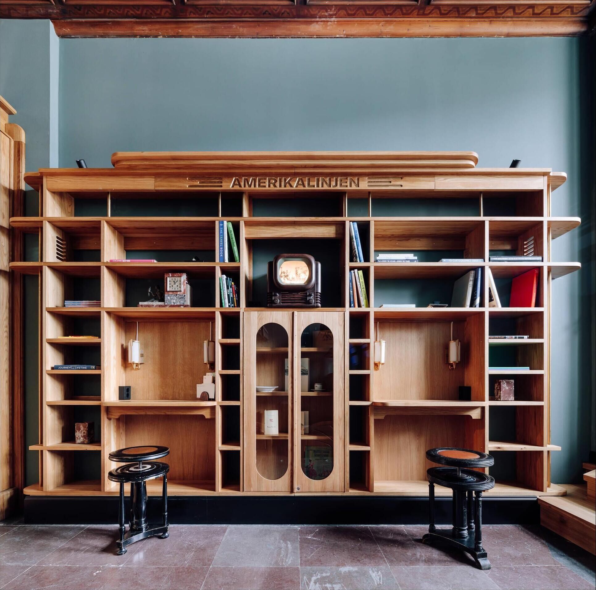 A spacious room with a large wooden bookshelf, two black stools, and a vintage television.