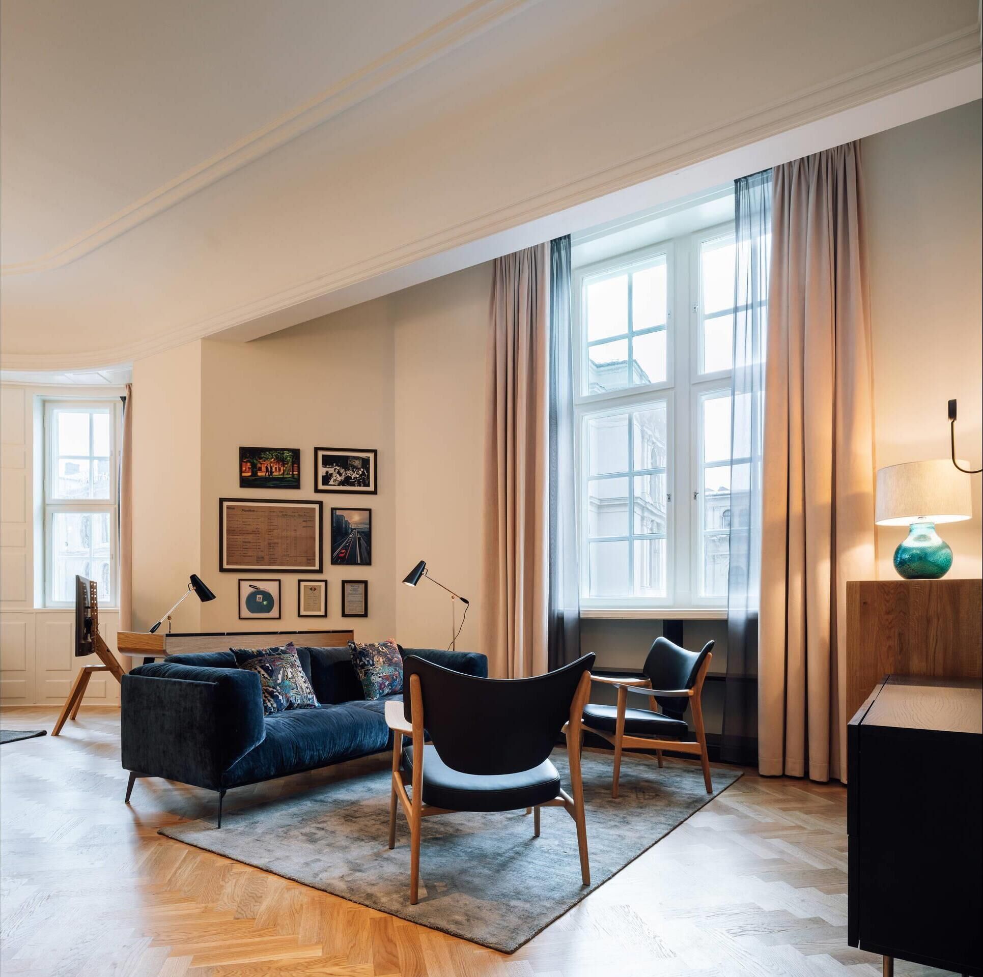 A modern living room with a blue sofa, two chairs, a coffee table, and a large window with curtains.