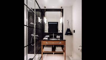 Un baño moderno con cabina de ducha de vidrio, tocador de madera con espejo y lámpara colgante negra.