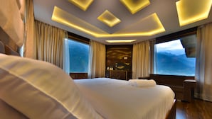 Habitación de hotel moderna con una cama grande, un área de descanso y vistas a montañas a través de las ventanas.