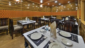 Un restaurante con paneles de madera y un techo estampado. Las mesas están listas con platos, cubiertos y botellas de agua.