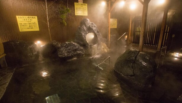 A hot spring bath area with large rocks, steam, and wooden architecture. - Kur and Hotel Shinshu (Shiojiri)