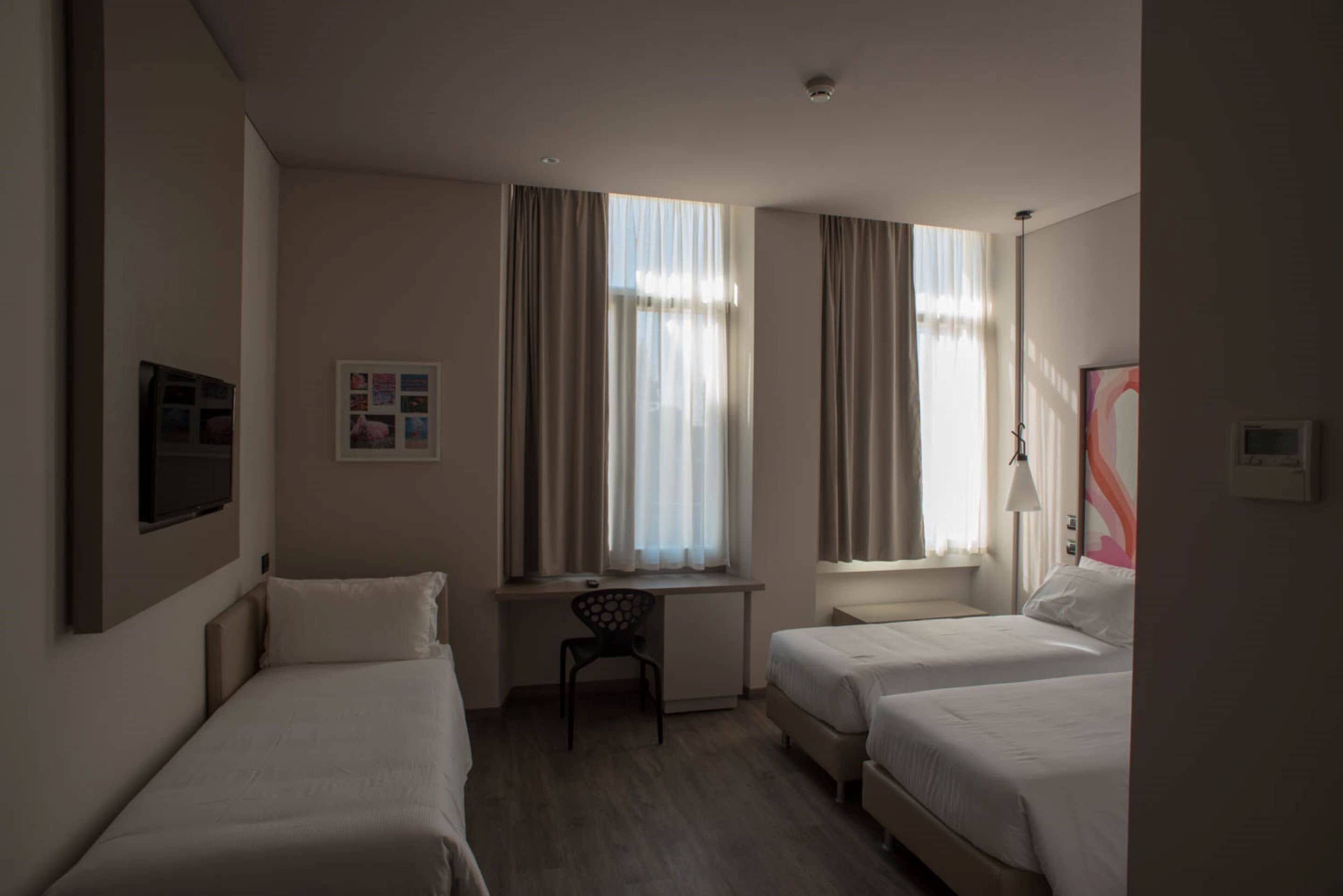 A hotel room with two single beds, a desk, a chair, and a television on the wall.