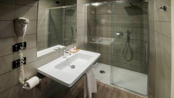 Un baño moderno con ducha envuelta en vidrio, un lavabo blanco y un secador de pelo fijado a la pared.