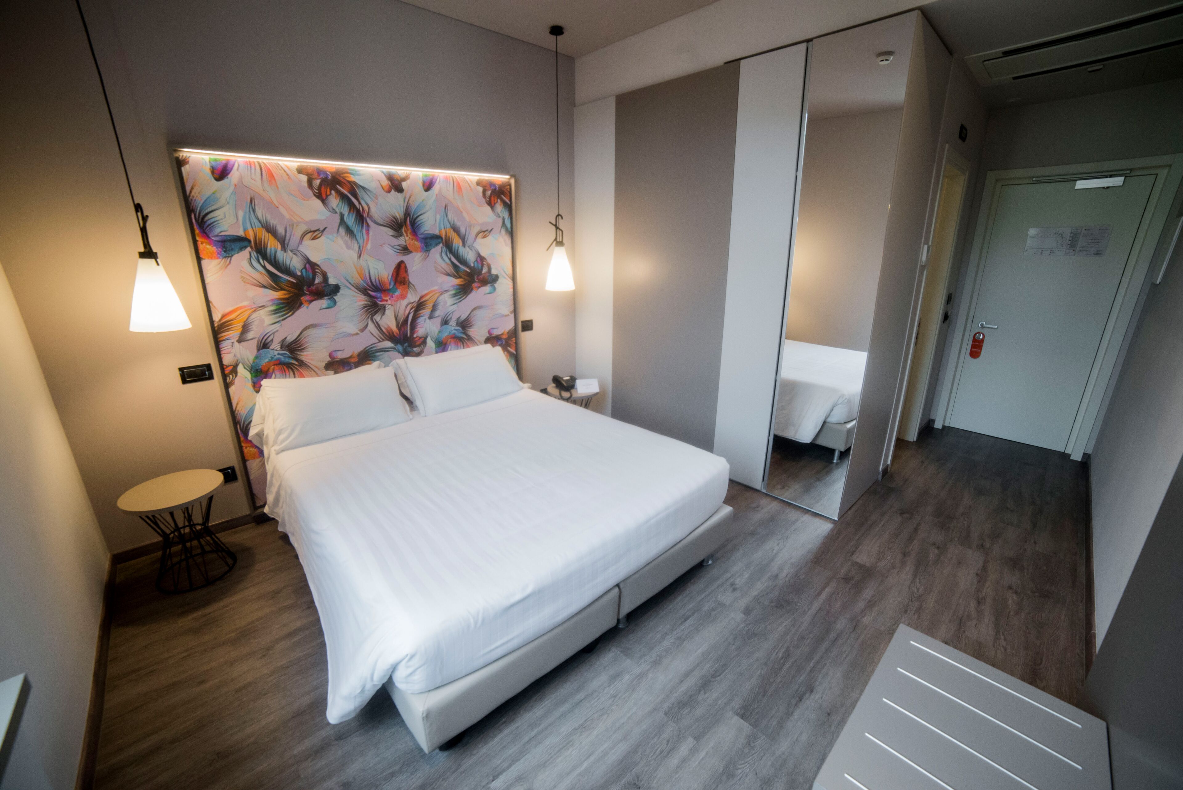 Een moderne hotelkamer met een groot bed, een klein rond tafeltje en een spiegelkast.
