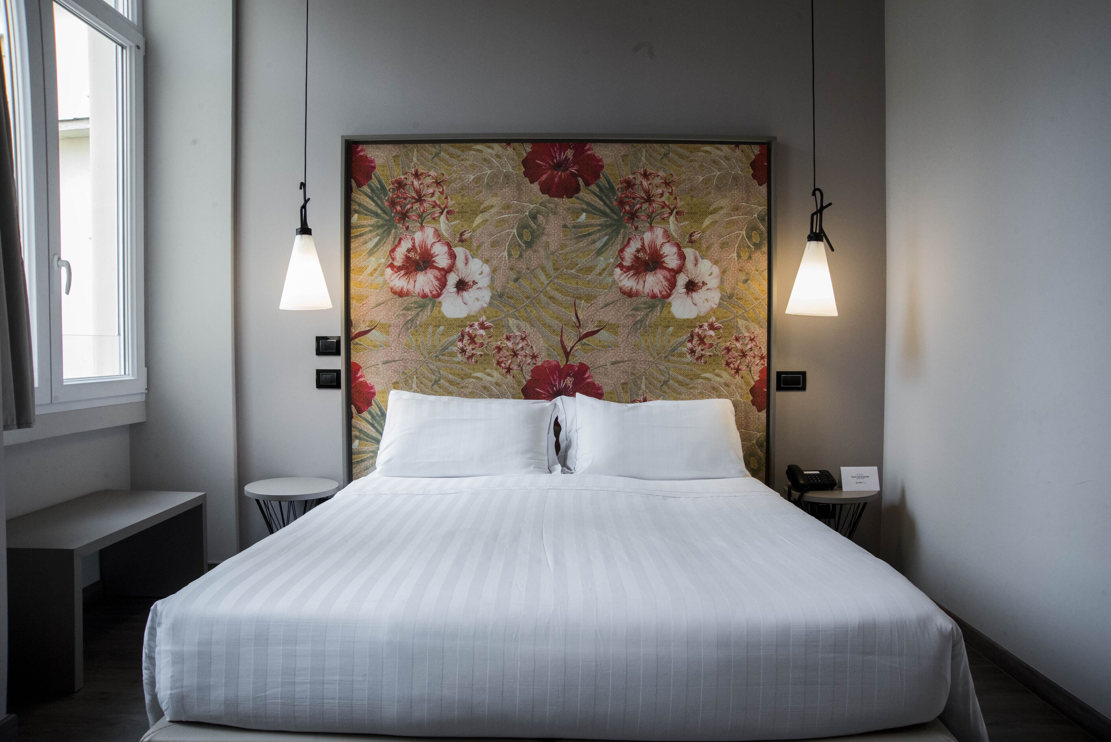 A hotel room with a large bed, two bedside lamps, a small table, and a window.