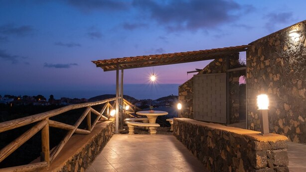 Eine Terrasse mit Steinwänden und einer Holzw pergola, einem runden Tisch und einer Bank.