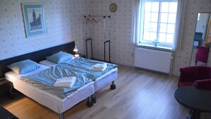 A neatly made bed with pillows, a bedside table with a lamp, a window with curtains, and a chair. - Abild Hotel (Tonder)