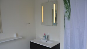 A bathroom with a white sink, a mirror, a shelf with a cup, and a bottle of hand soap. - Abild Hotel (Tonder)