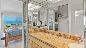 Une salle de bain moderne dotée d’un grand miroir, d’un comptoir en granit et offrant une vue sur l’océan par la porte ouverte.
