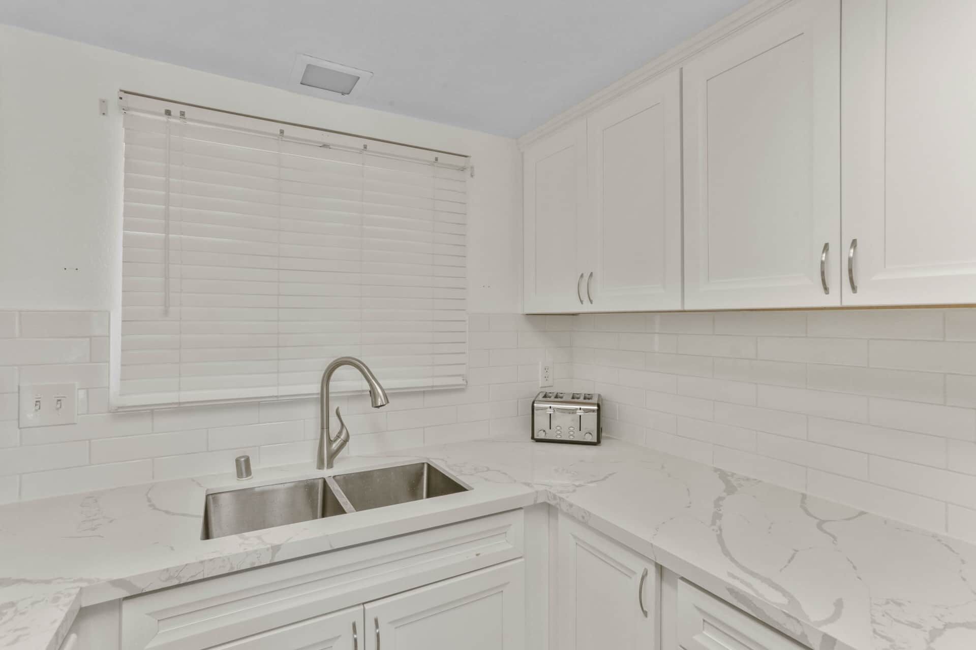 A kitchen with white cabinets, a stainless steel sink, a marble countertop, and a toaster.