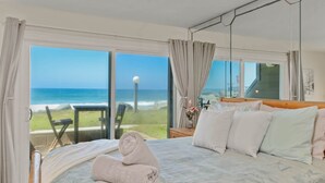 Une chambre avec un grand lit, une vue sur l’océan et un balcon équipé d’une table et de chaises.