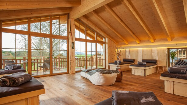 A spacious wooden interior with large windows, a wooden deck outside, and seating areas with cushions. - Hotel Rupertihof (Ainring)