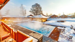 A heated outdoor pool area with wooden deck seating and snow-covered surroundings. - Hotel Rupertihof (Ainring)