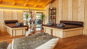 A cozy room with wooden walls and ceiling, a sofa bed, a small table, and a bookshelf. - Hotel Rupertihof (Ainring)