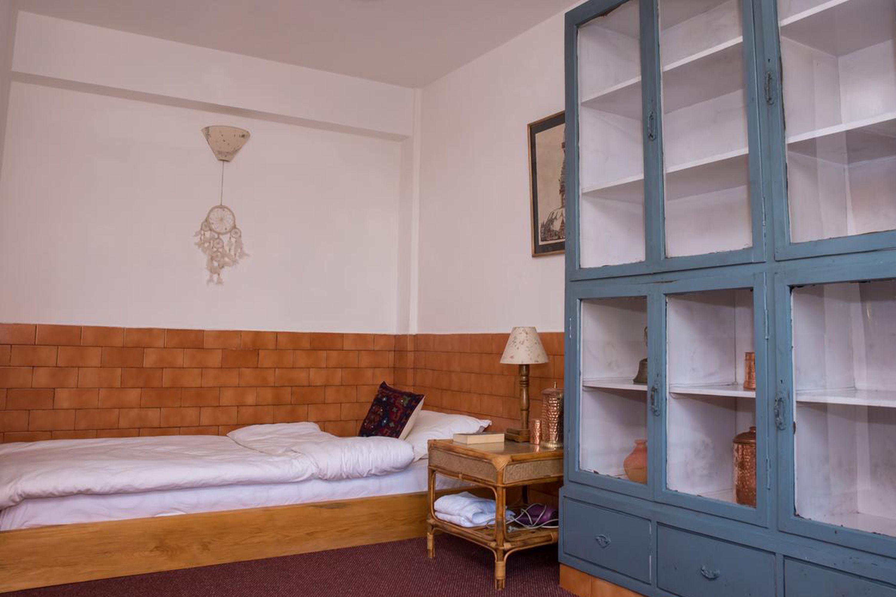 A bedroom with a wooden headboard, a bed with white bedding, a bedside table with a lamp, and a blue cabinet with shelves.