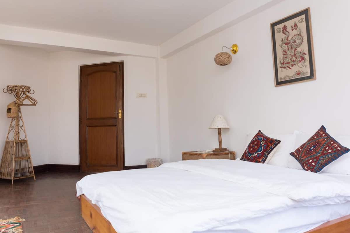A bedroom with a wooden bed, a door, a wall-mounted lamp, and a framed artwork.