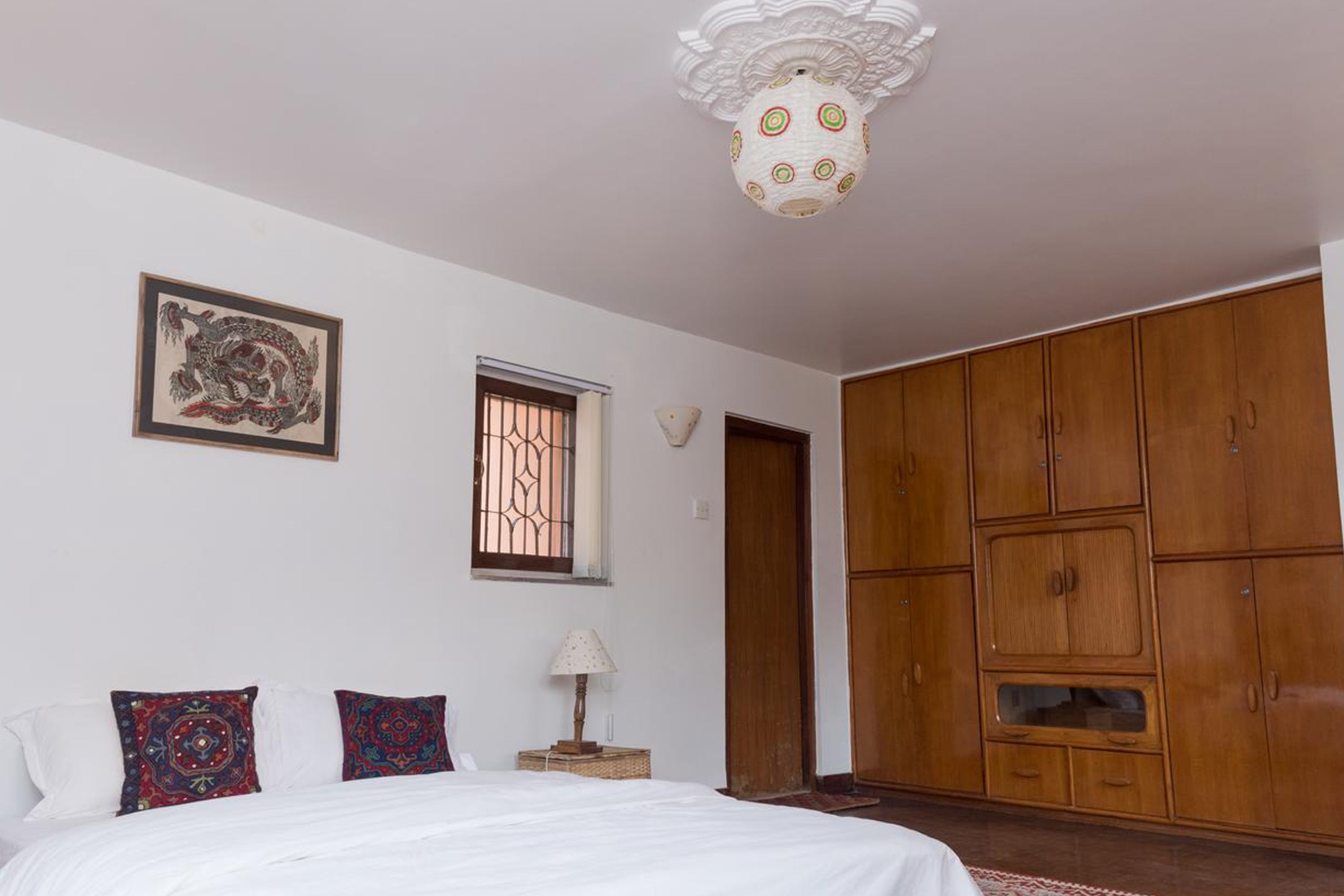 Un dormitorio con una cama, un armario de madera, una lámpara decorativa en el techo y una obra de arte enmarcada en la pared.