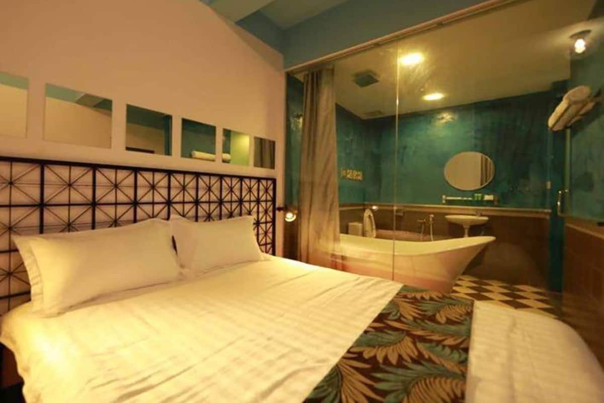A hotel room with a bed, a large mirror, a bathtub, and a window with curtains.