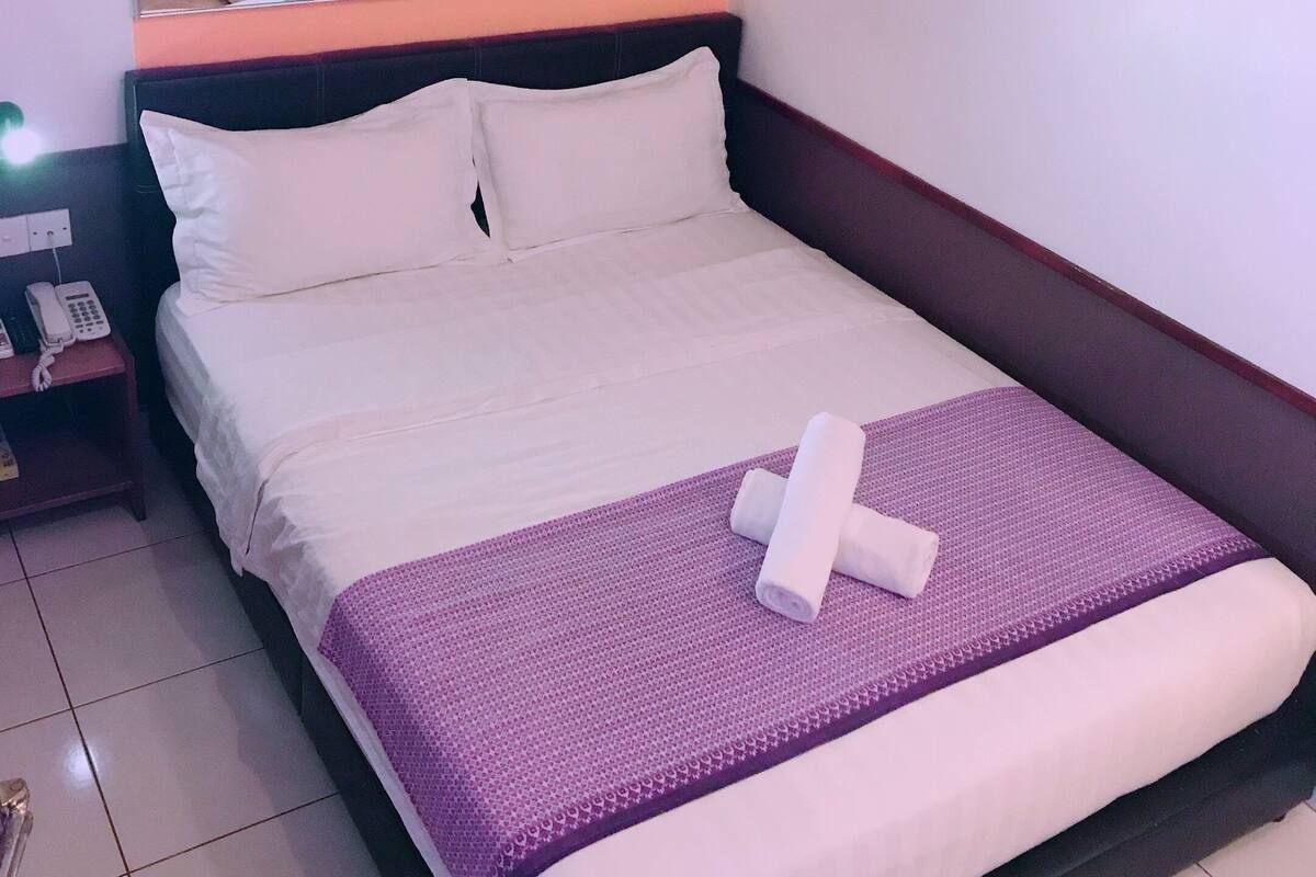 A neatly made bed with white linens, a purple blanket, and a rolled towel. There is a telephone on a nightstand beside the bed.