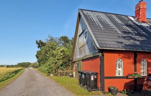 A rural road leading to a red building with a black roof, a wooden fence, and a trash bin. - 2 bedroom awesome home in østermarie (Østermarie)