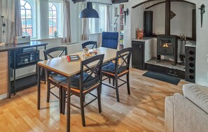 Una sala de estar acogedora con piso de madera, una mesa de comedor con sillas, un sofá, una chimenea y una zona de cocina con microondas y hervidor.