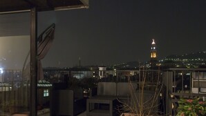 A rooftop terrace with outdoor furniture, a potted plant, and a view of a distant tower. - Alex e Angie (Bergamo)