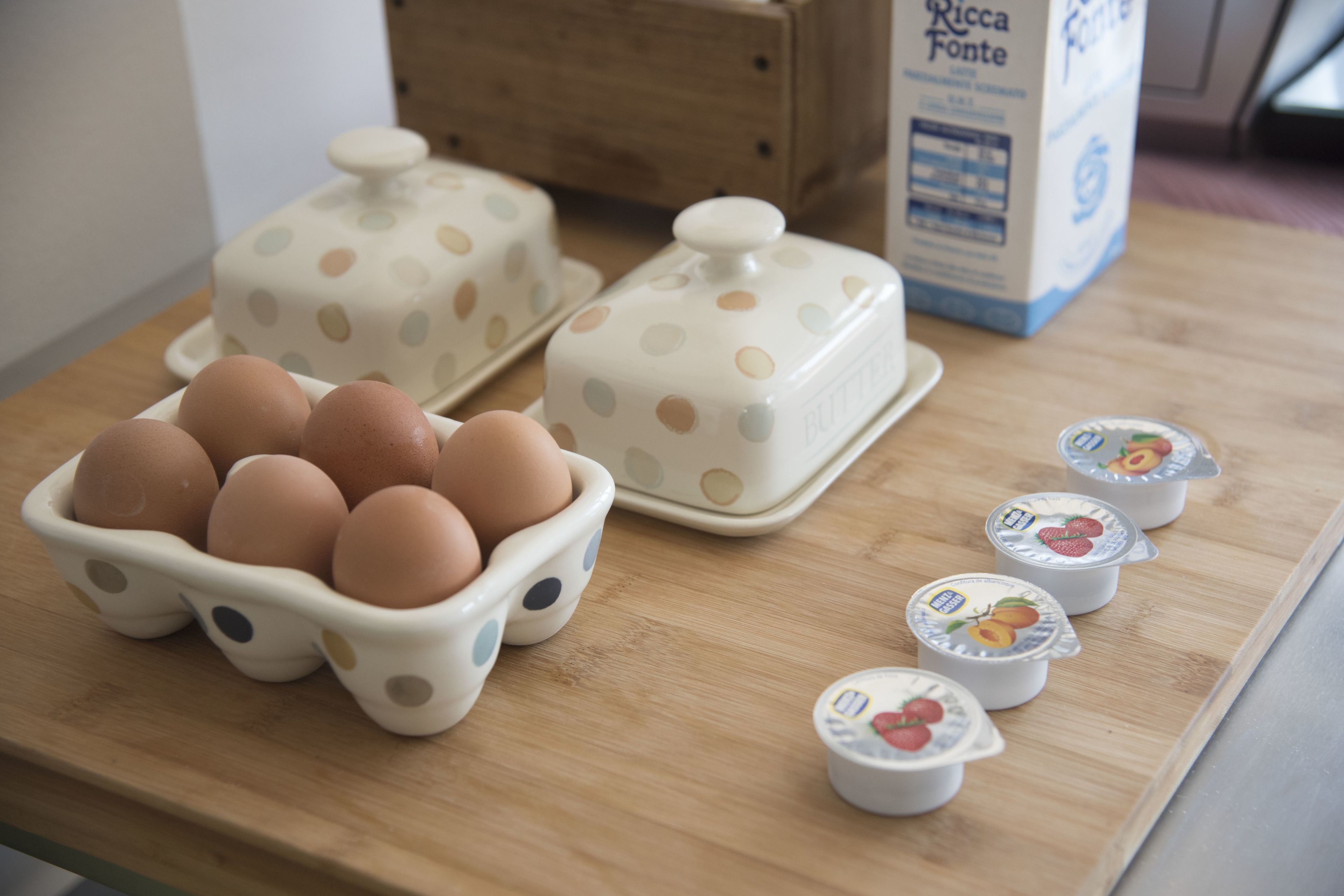 A wooden table with a carton of eggs, two polka-dotted containers, and a carton of Ricca Fonte milk.