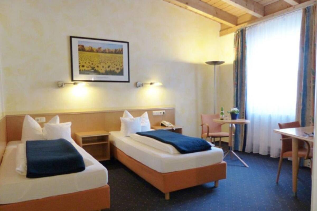 Ein Hotelzimmer mit zwei Betten, einem Schreibtisch, einem Stuhl und einem Bild an der Wand.