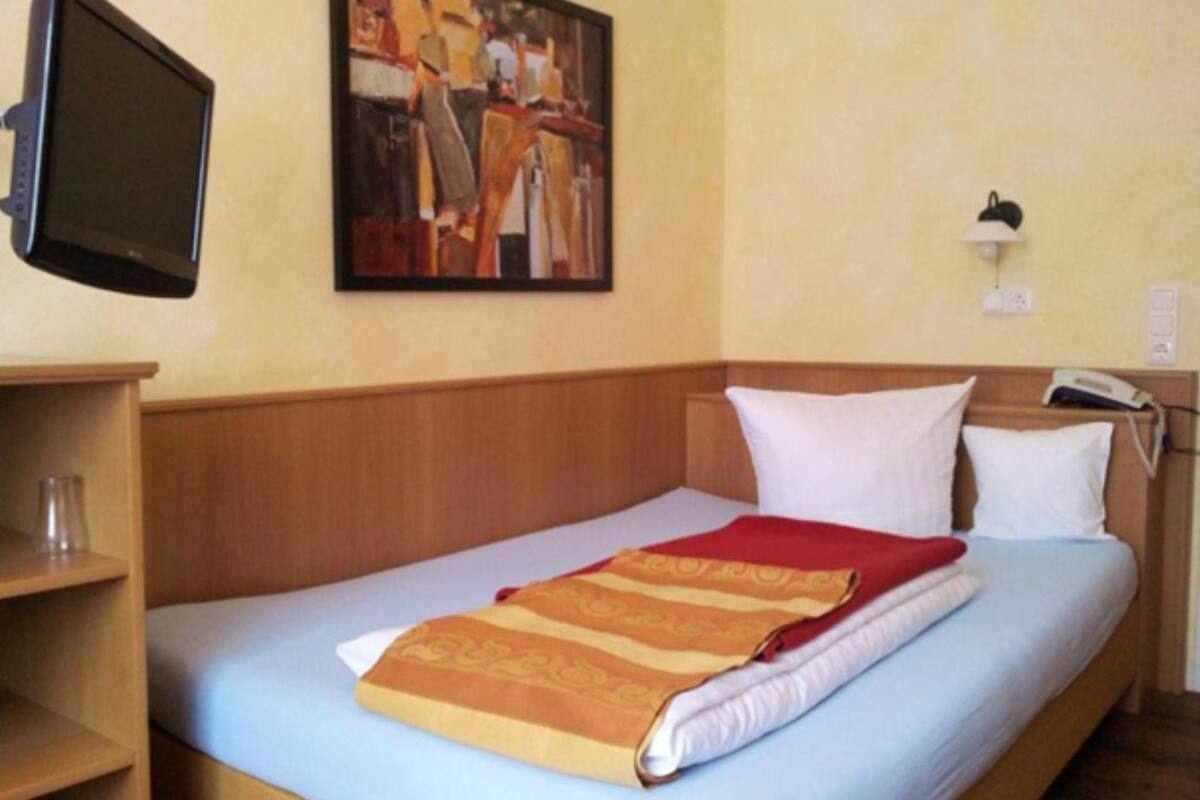 Ein Hotelzimmer mit Bett, einem Bild an der Wand, einem Schreibtisch mit Computer und Telefon.