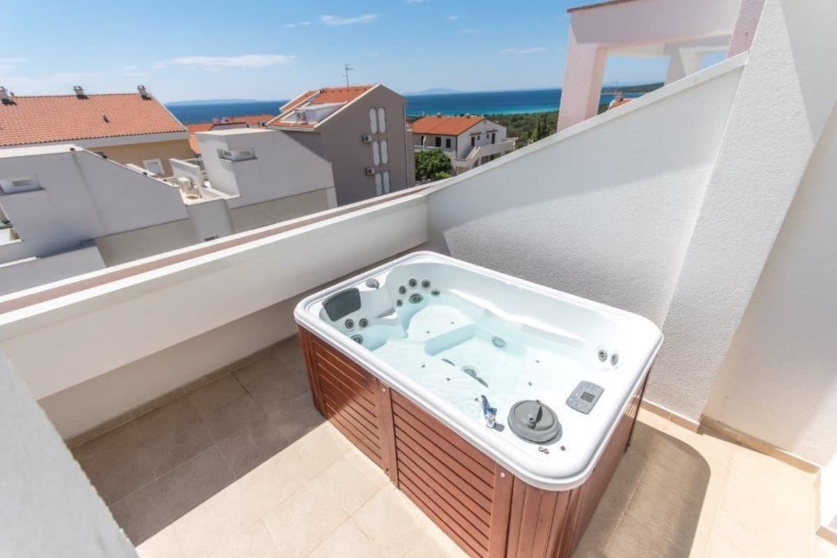 A balcony with a hot tub, a view of the sea, and neighboring buildings.