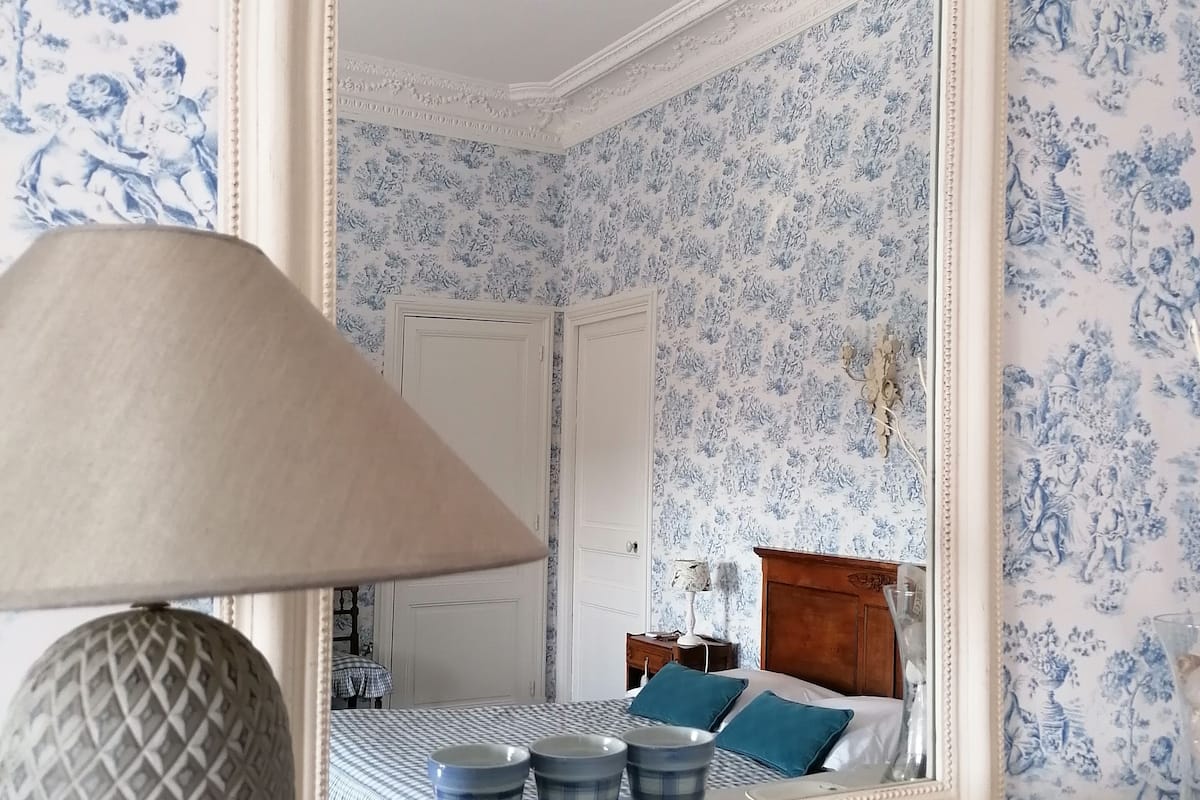 A bedroom with a large mirror, a lamp, and a bed with blue and white checkered bedding.