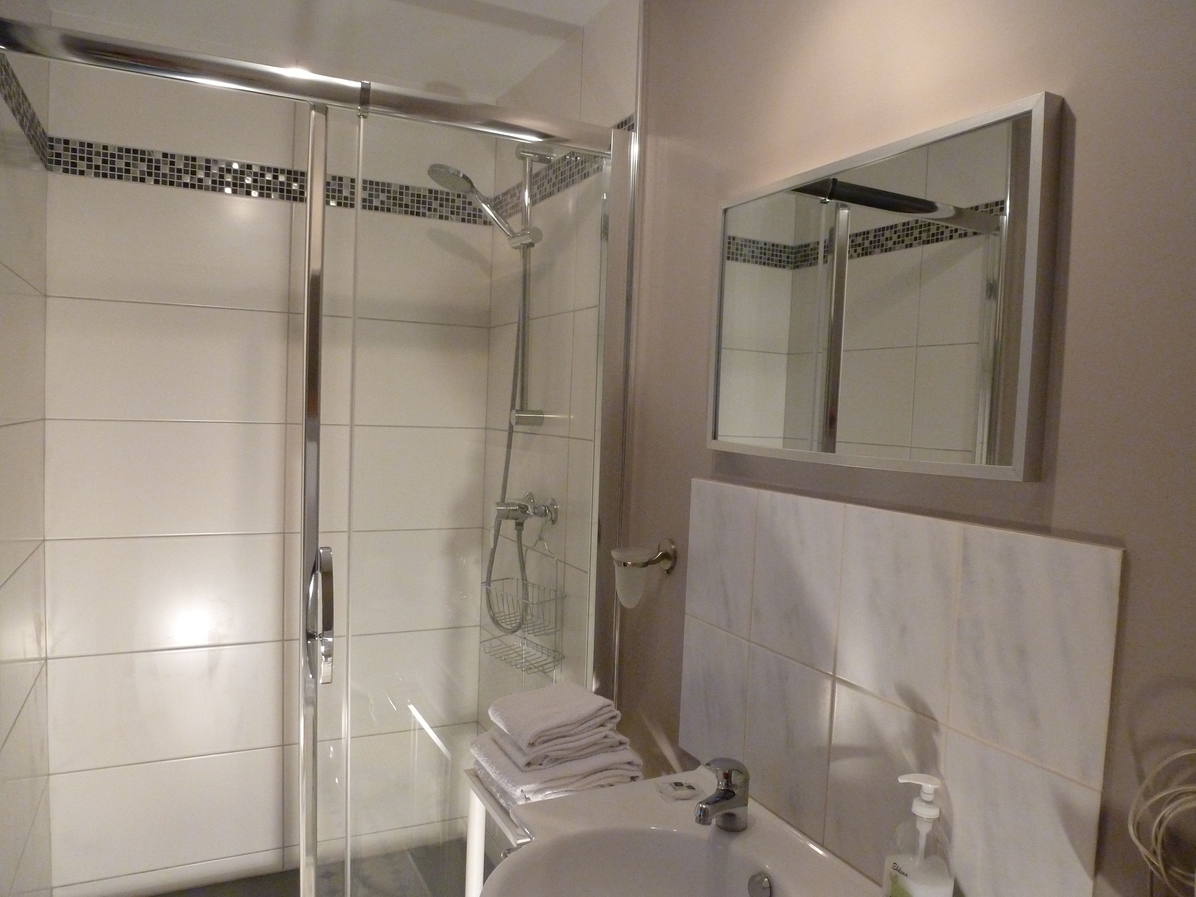 A bathroom with a glass-enclosed shower, a sink with a mirror above it, and a towel rack with folded towels.