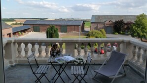 A balcony with a table, chairs, and a view of farm buildings and fields. - Ferme de Bonavis - Chambres d'Hôtes (Banteux)